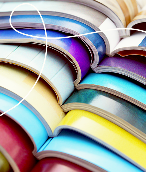 Ein Bild von vielen bunten Zeitschriften die aufeinander liegen und durch die Falt in der Mitte eine Linie von links nach rechts ergeben dazu oben links eine helle geschwungene Linie als Gestaltungselement | Kremer Signature Design