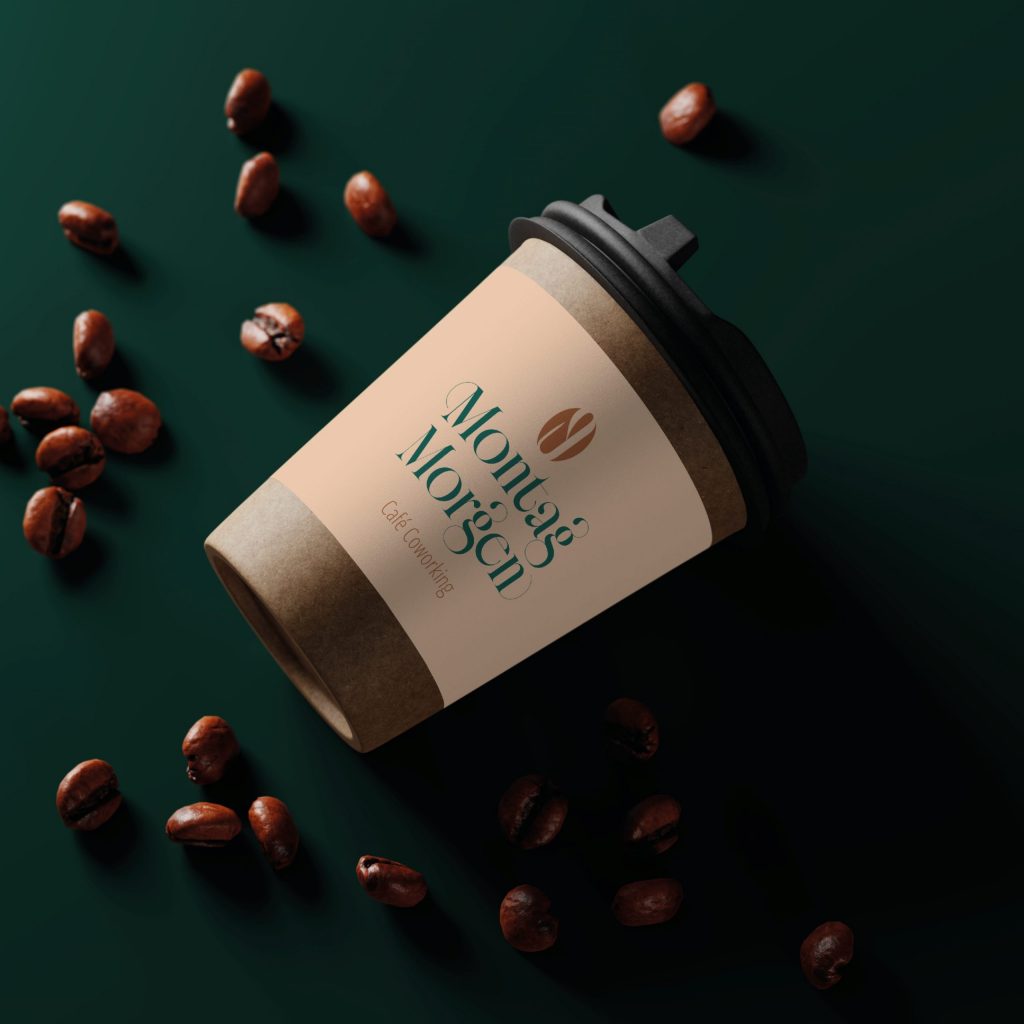 Mockup-Darstellung eines Kaffeebechers zum Mitnehmen auf dunkel grünem Hintergrund mit frei rumliegenden Kaffeebohnen, ergibt eine sehr warme und edle Atmosphäre. Brand Name lautet: Montagmorgen | Kremer Signtaure Design